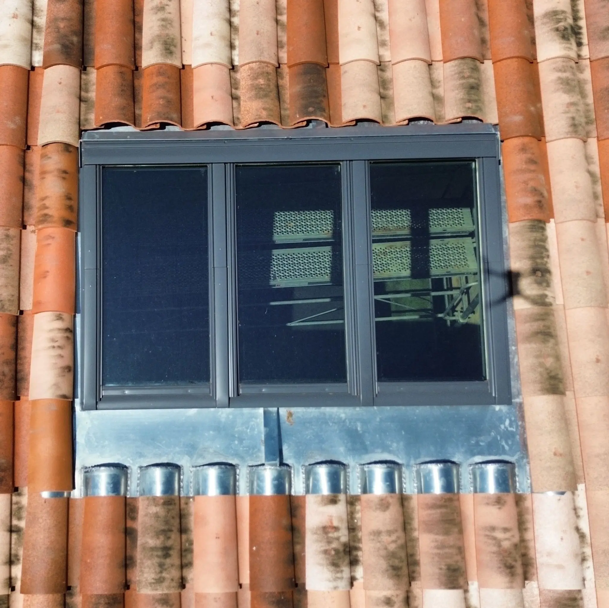 Lucarne en zinc avec des fenêtres en bois, intégrée dans un toit en tuiles rouges, ajoutant une touche traditionnelle à l'architecture