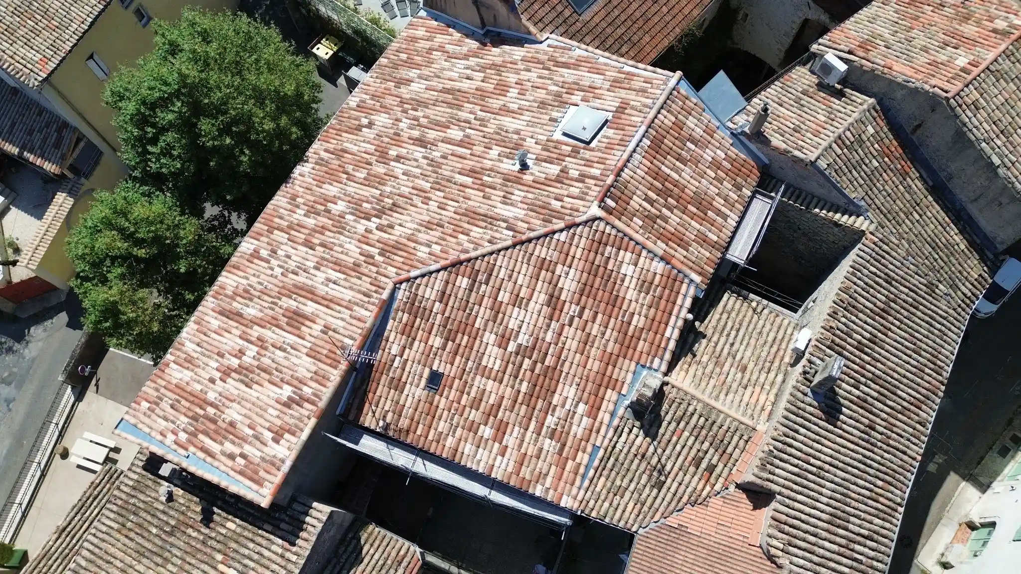 Drôme, vue de dessus d'un toit en tuiles vieillies rouges et blanches, montrant la structure détaillée du toit et les bâtiments adjacents.