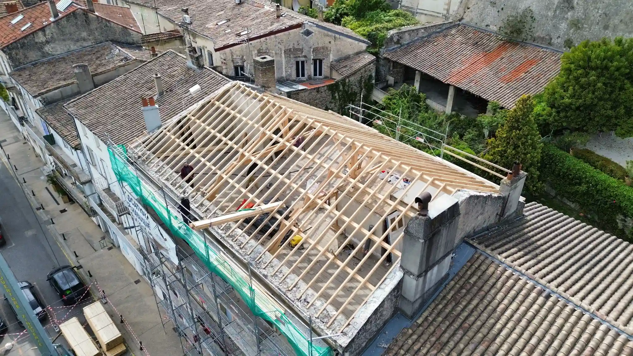 Vue aérienne d'une rénovation de toiture sur un ancien bâtiment, montrant des poutres en bois neuves en cours d'installation dans la structure du toit.