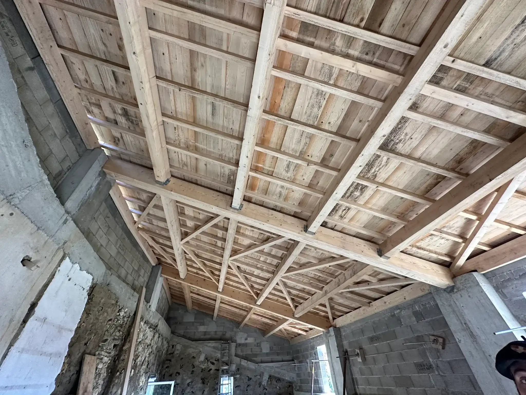 Nouveau plafond en bois dans un bâtiment, composé de poutres et de supports en bois, avec des murs inachevés.