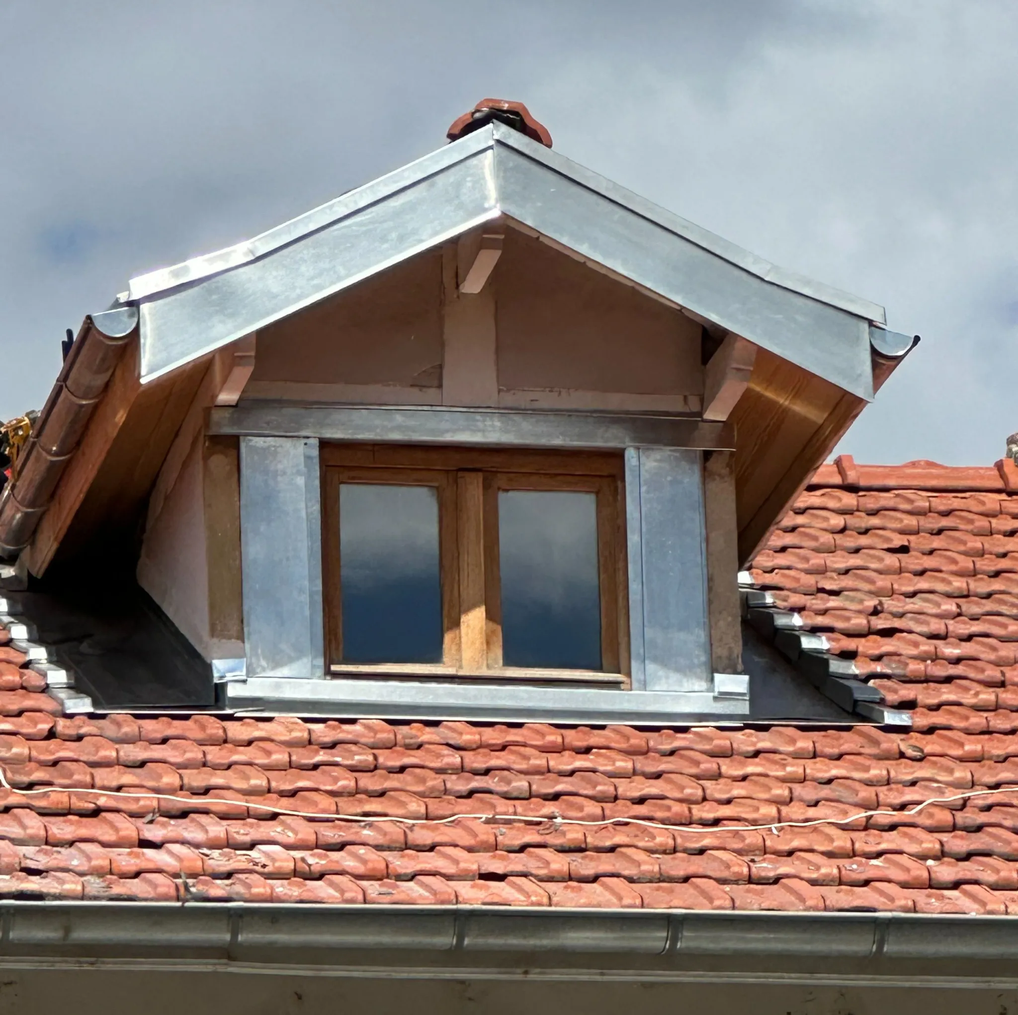 Fenêtre de toit moderne installée dans un cadre en zinc, entourée de tuiles rouges et brunes, permettant la lumière naturelle d’entrer dans l’intérieur.